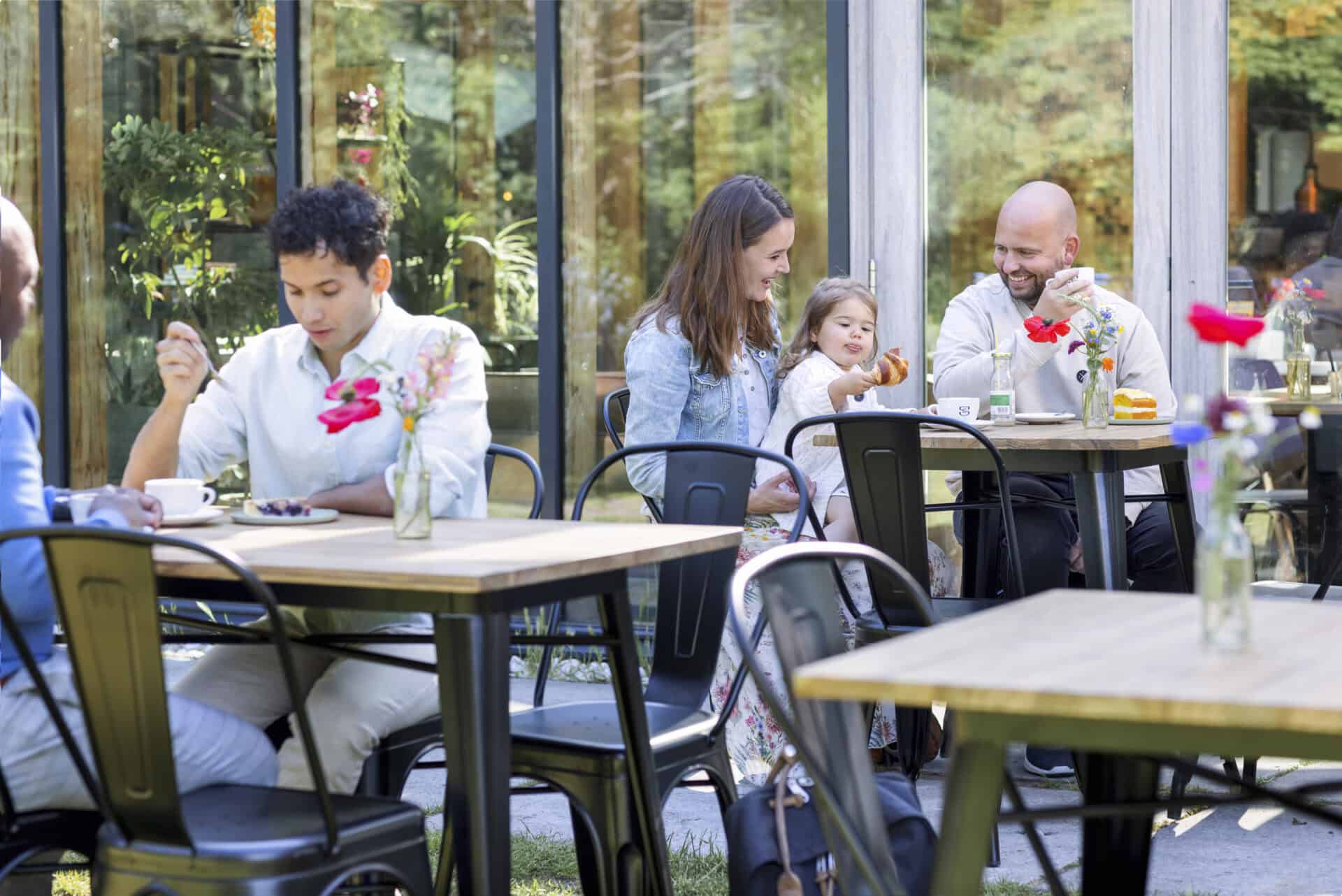 Gezellig terras met statafels en familie genieten buiten.