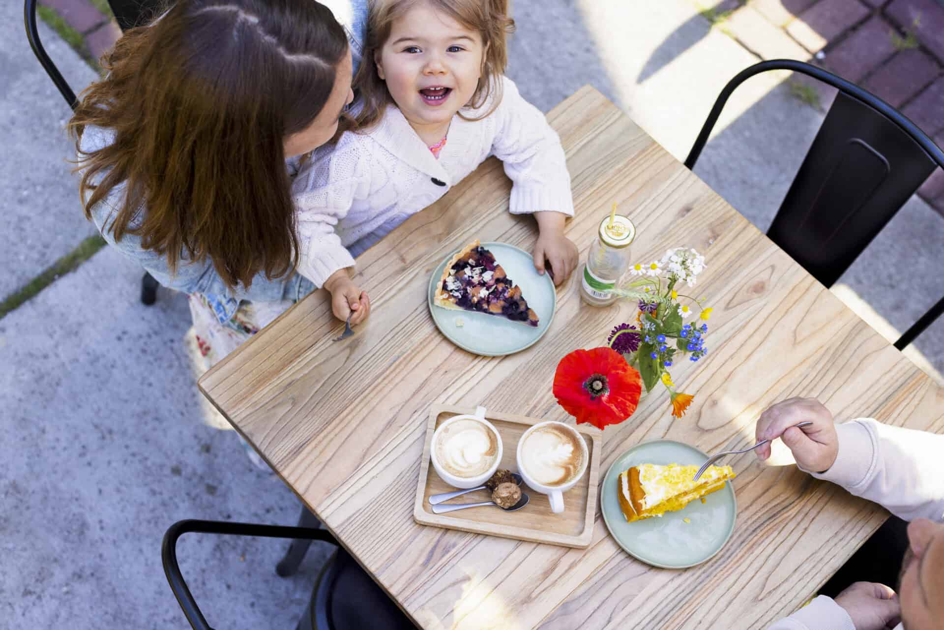 Gezellig terras met statafels en kinderen genieten van taart.